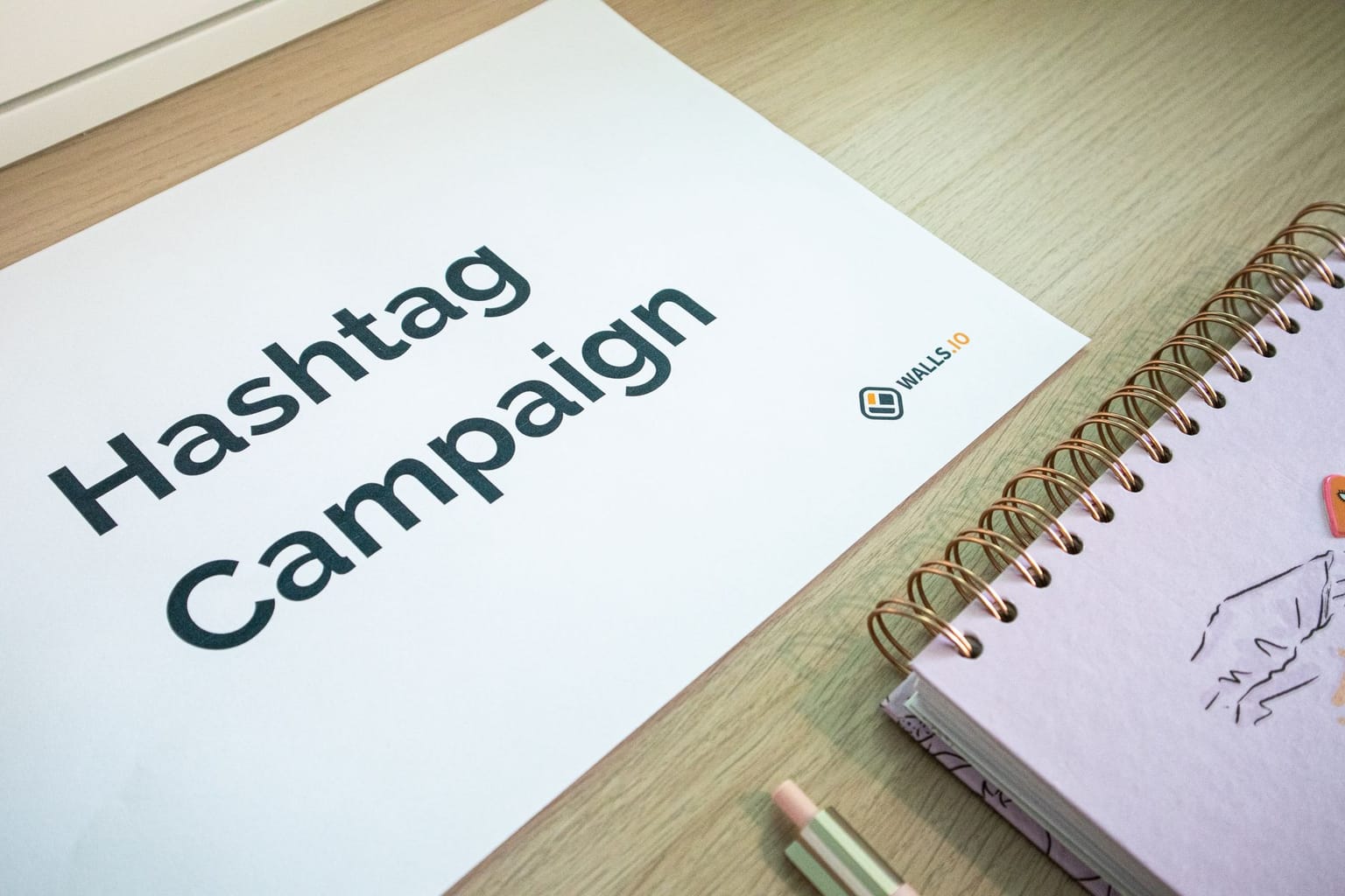 A paper with “Hashtag Campaign” printed on it lies on a desk next to a spiral notebook and a pencil