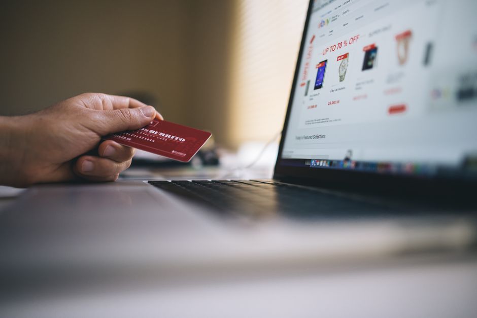 A person holds a credit card near a laptop, making an online purchase on a shopping website that displays discounts on software