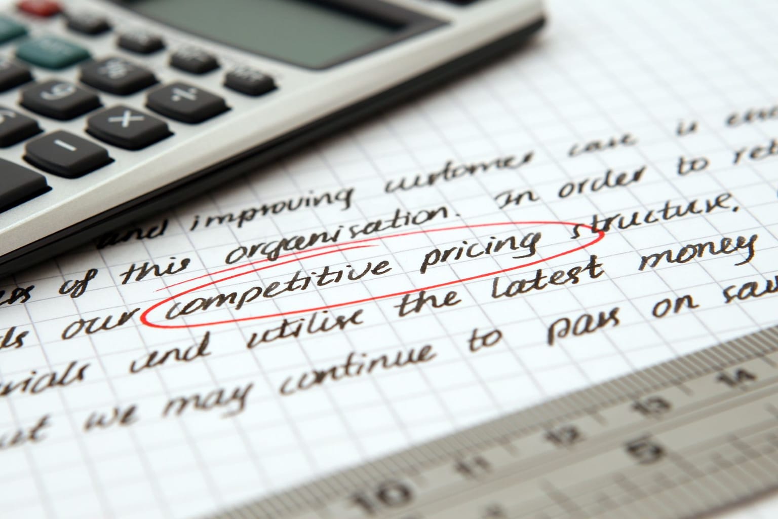 A close-up of handwritten notes on graph paper, with “competitive pricing” and “AppSumo pricing” circled in red. Part of a calculator and a ruler are