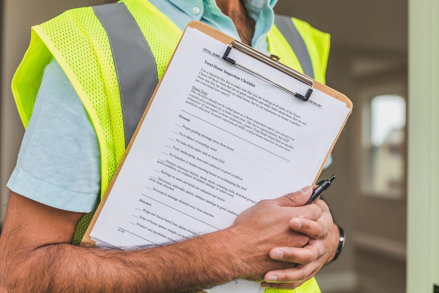 A person in a yellow safety vest holds a clipboard with a printed buyer checklist and a pen, standing indoors.