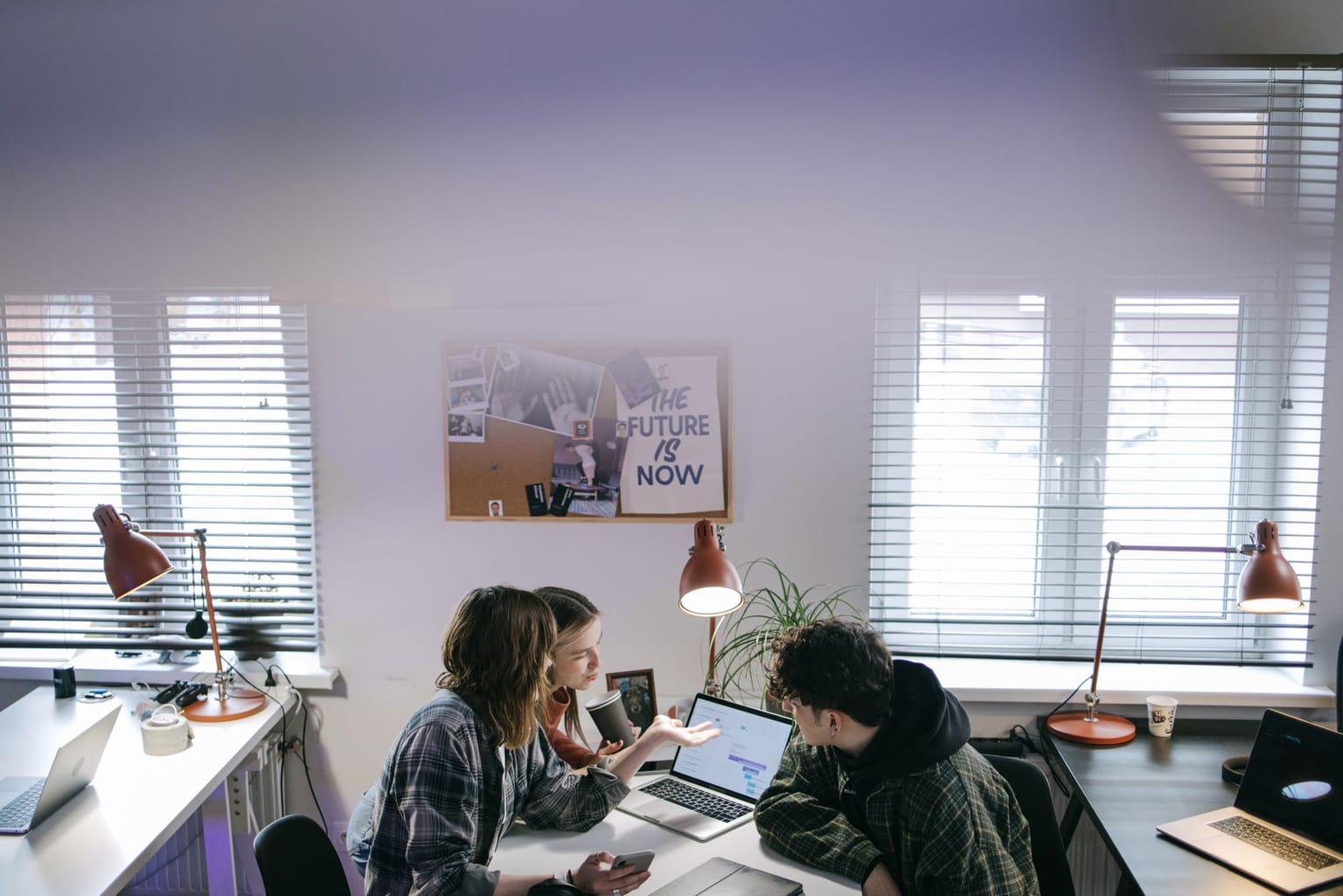 Three people sit around a desk with laptops and papers in a bright office, collaborating on their agency software stack