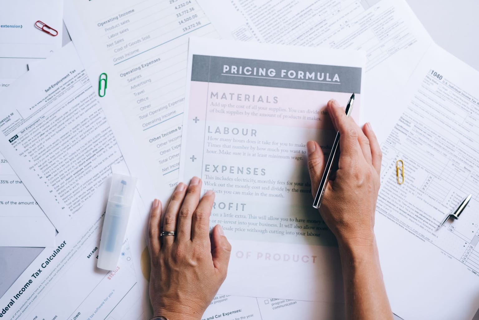 A person holds a printed pricing formula sheet over scattered financial documents