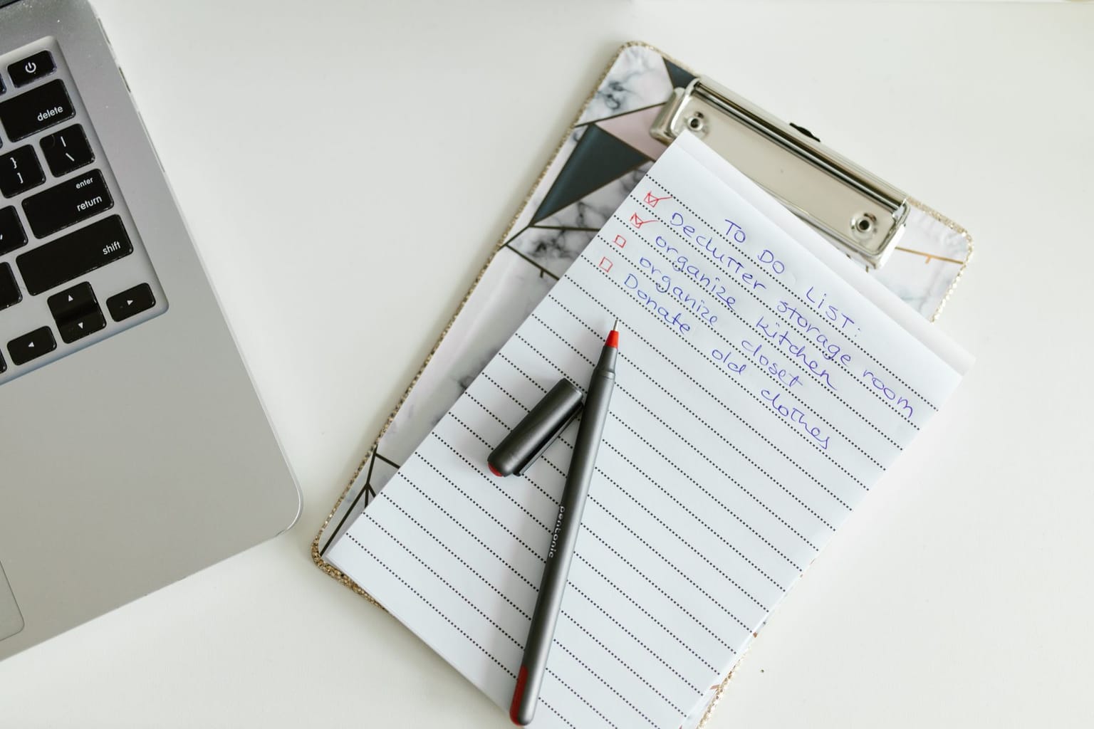 A notepad on a clipboard with a to-do list written in blue ink, a black and red pen resting on top