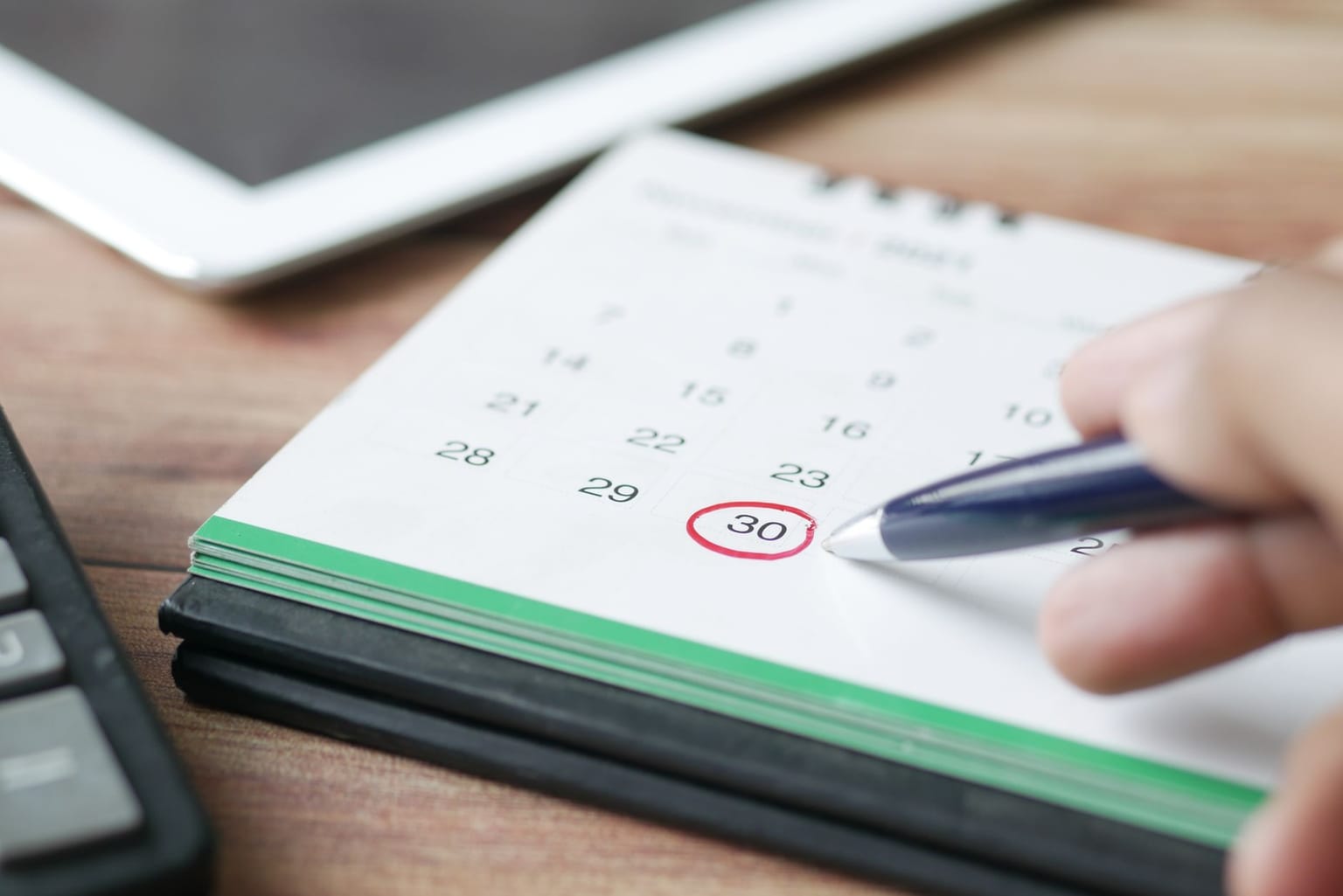 A hand holding a pen circles a date on a calendar, marking a refund deadline, with a calculator and tablet nearby