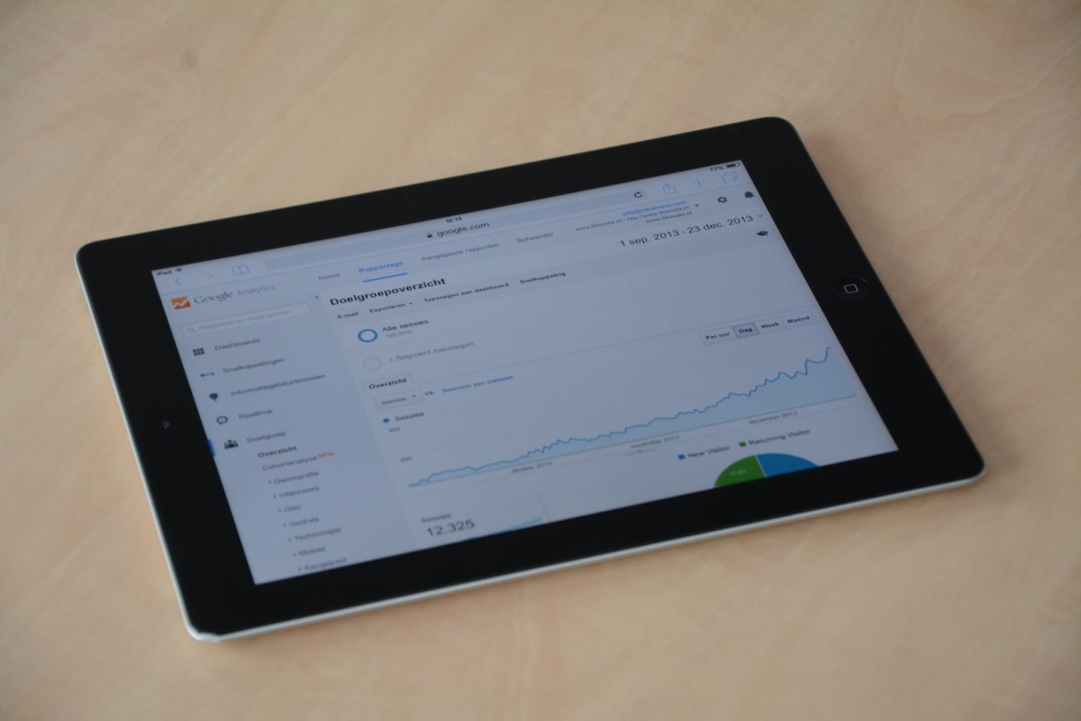 A black tablet on a light wooden surface displays an analytics dashboard with a line graph, a pie chart, and various statistics on the screen