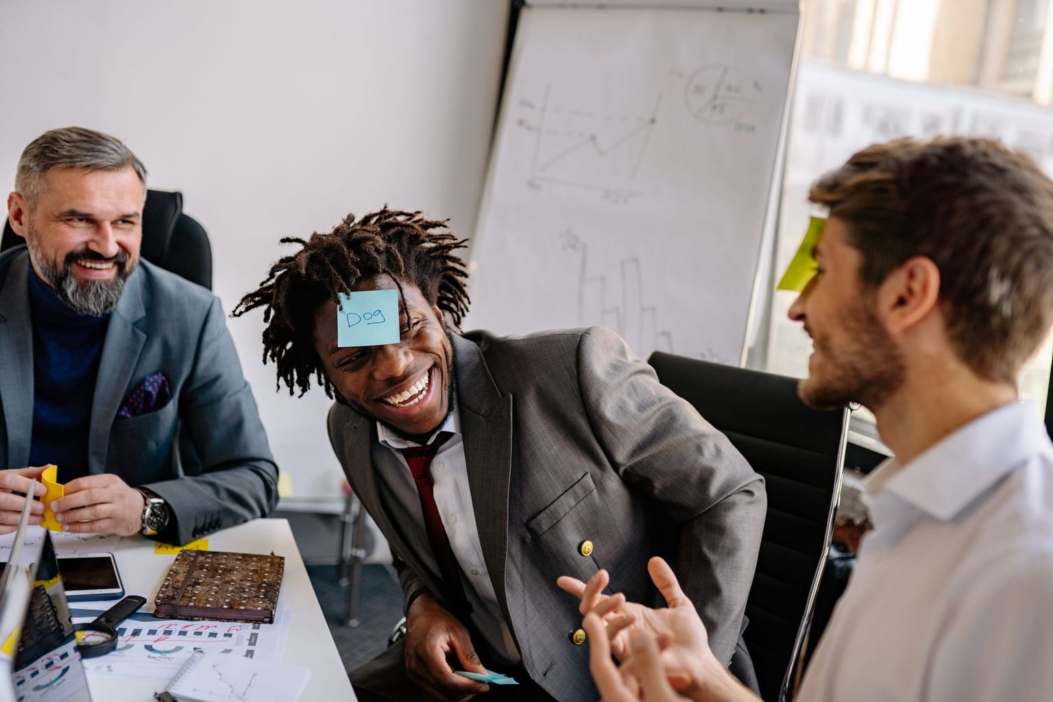 Three men in business attire laugh together in an office while playing a team icebreaker game