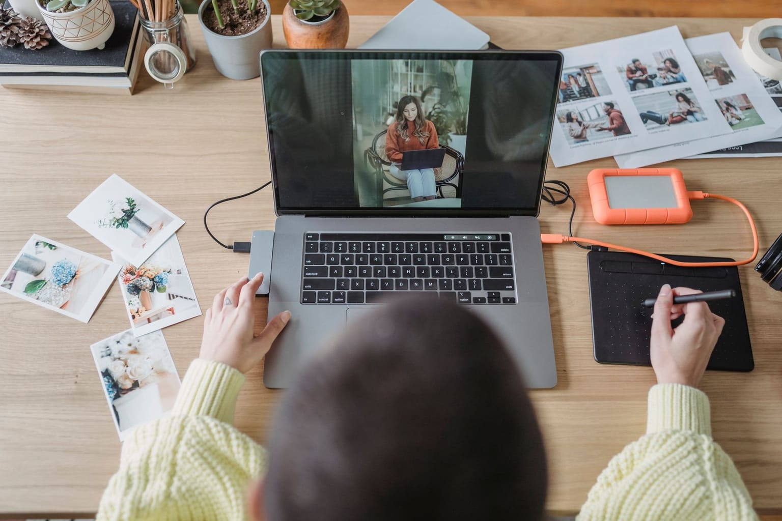 A person edits photos on a laptop using a graphics tablet, demonstrating a professional approach to photo editing. Printed photos, a hard drive