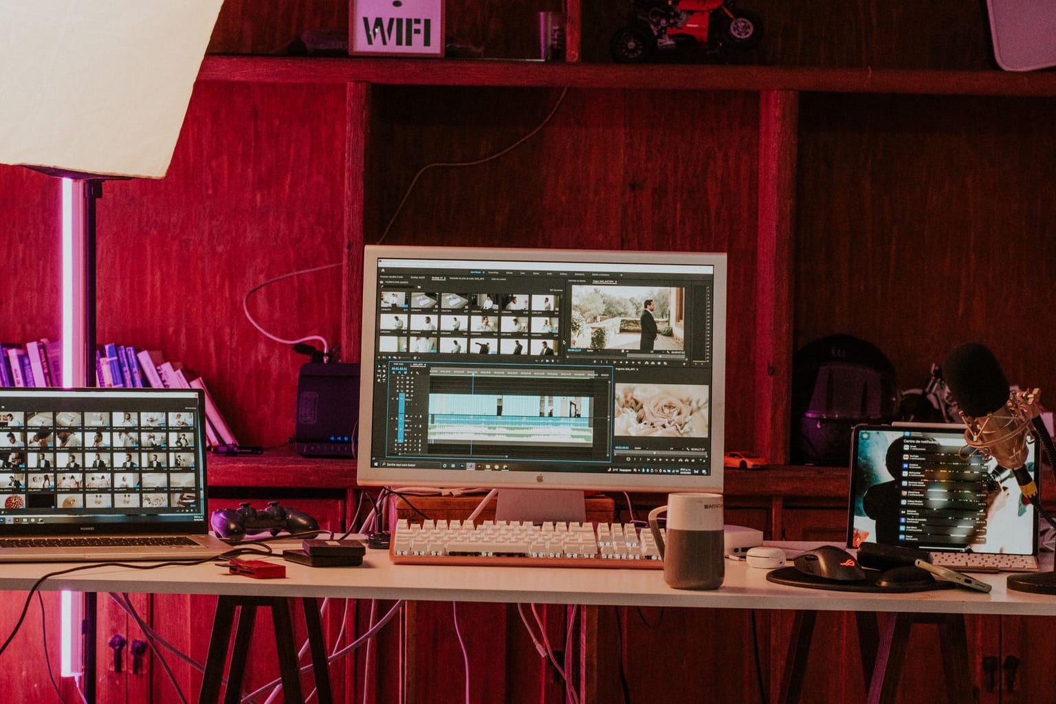 A desk with a laptop, monitor showing an online video editor, keyboard, headphones, microphone, coffee mug
