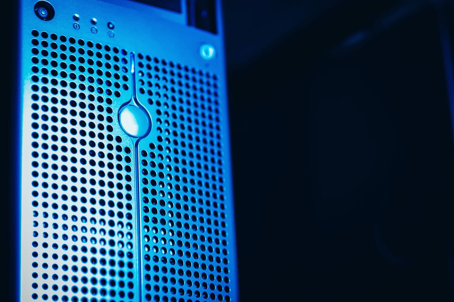 Close-up of a computer server tower with a perforated metal front panel, illuminated by blue light
