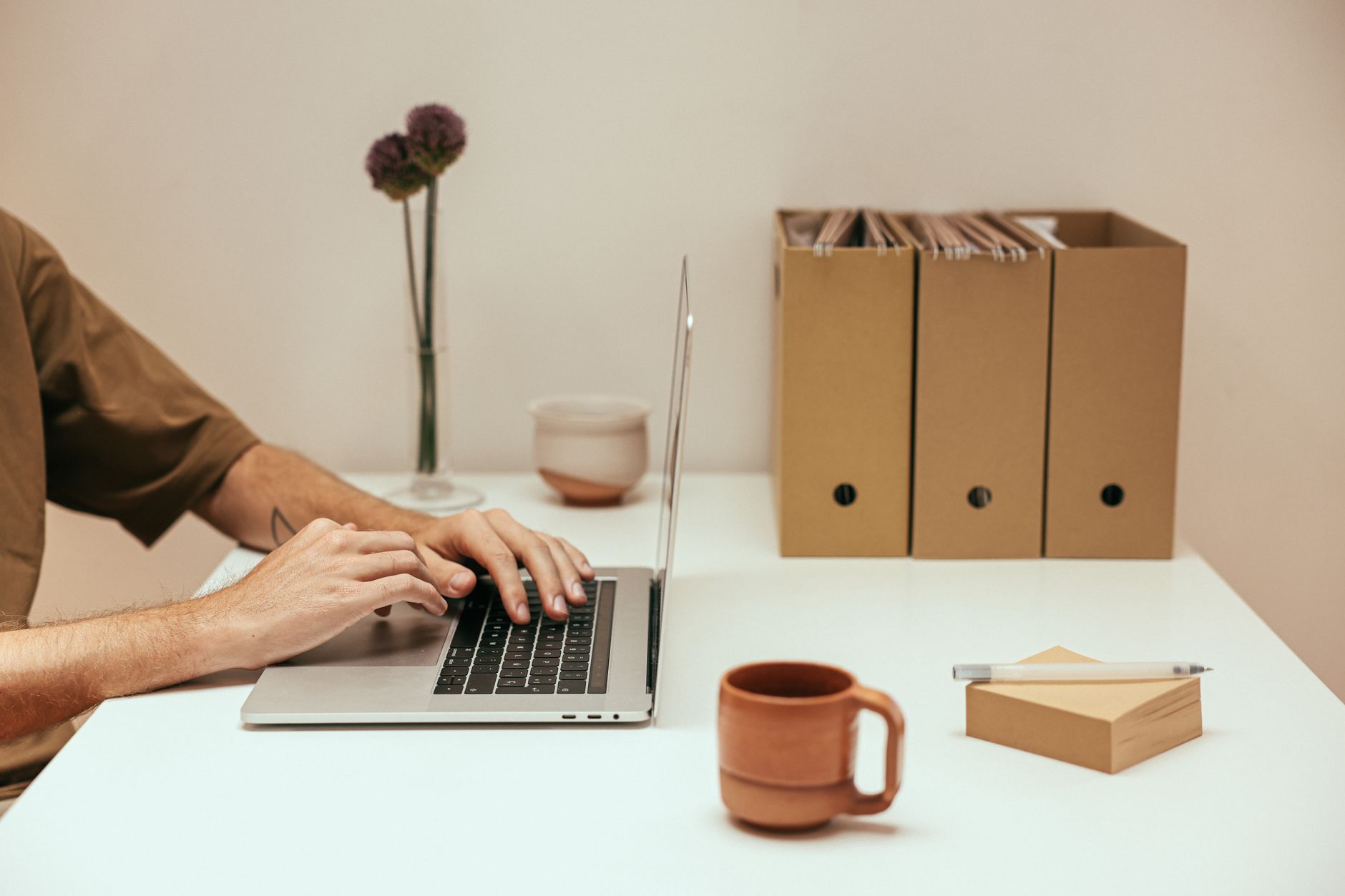 Hands typing on a laptop beside file organisers, the tidy stack a Koofr buyer should keep of what they have bought