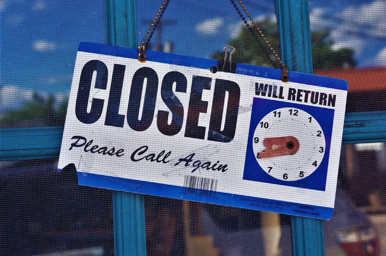 A “CLOSED” sign with “Please Call Again” hangs on a door, reminiscent of a shop awaiting new innovations like advanced checkout software. A clock