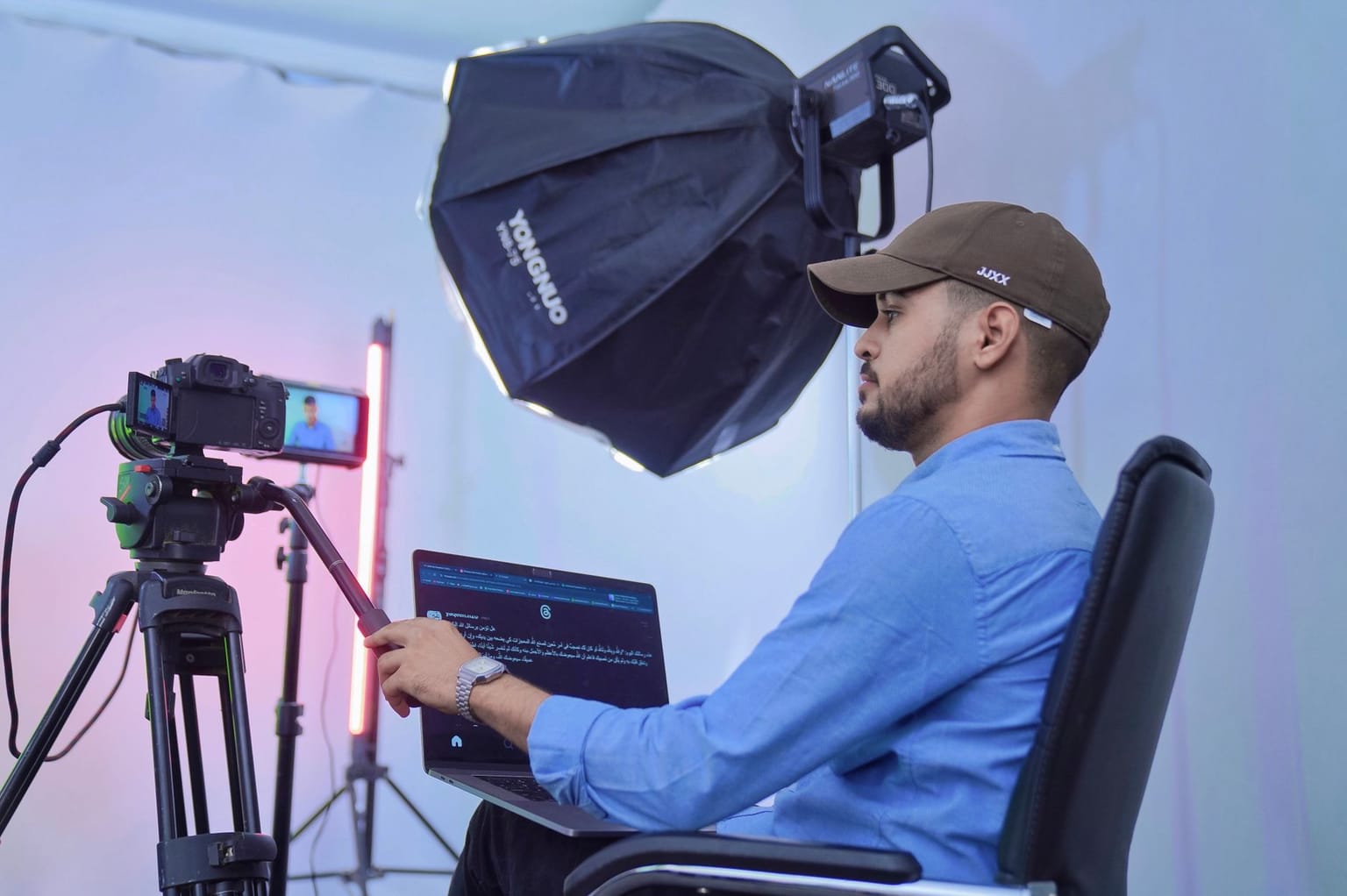 A person in a blue shirt and cap sits in front of a camera and laptop, possibly utilizing AI video tools like the Pictory lifetime deal