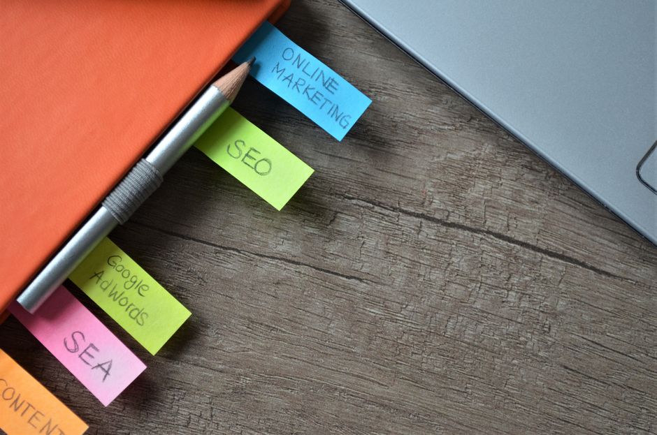A notebook with colourful sticky notes about online marketing, SEO and search ads sits on a wooden desk beside a pencil