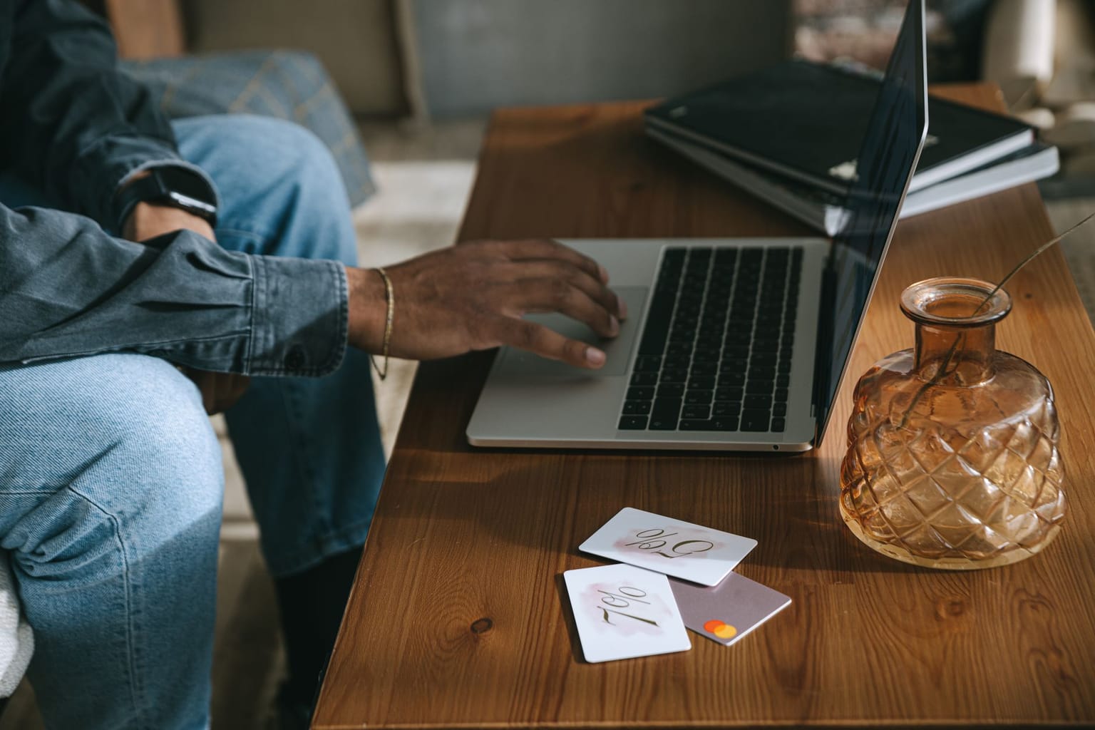 A person using a laptop at a wooden table with two cards showing percentage signs, suggesting an online software discount