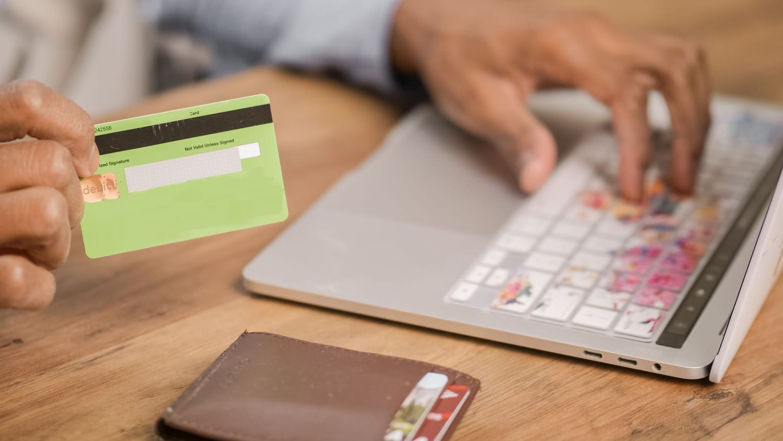 A person holding a green credit card in one hand while typing on a laptop keyboard with the other