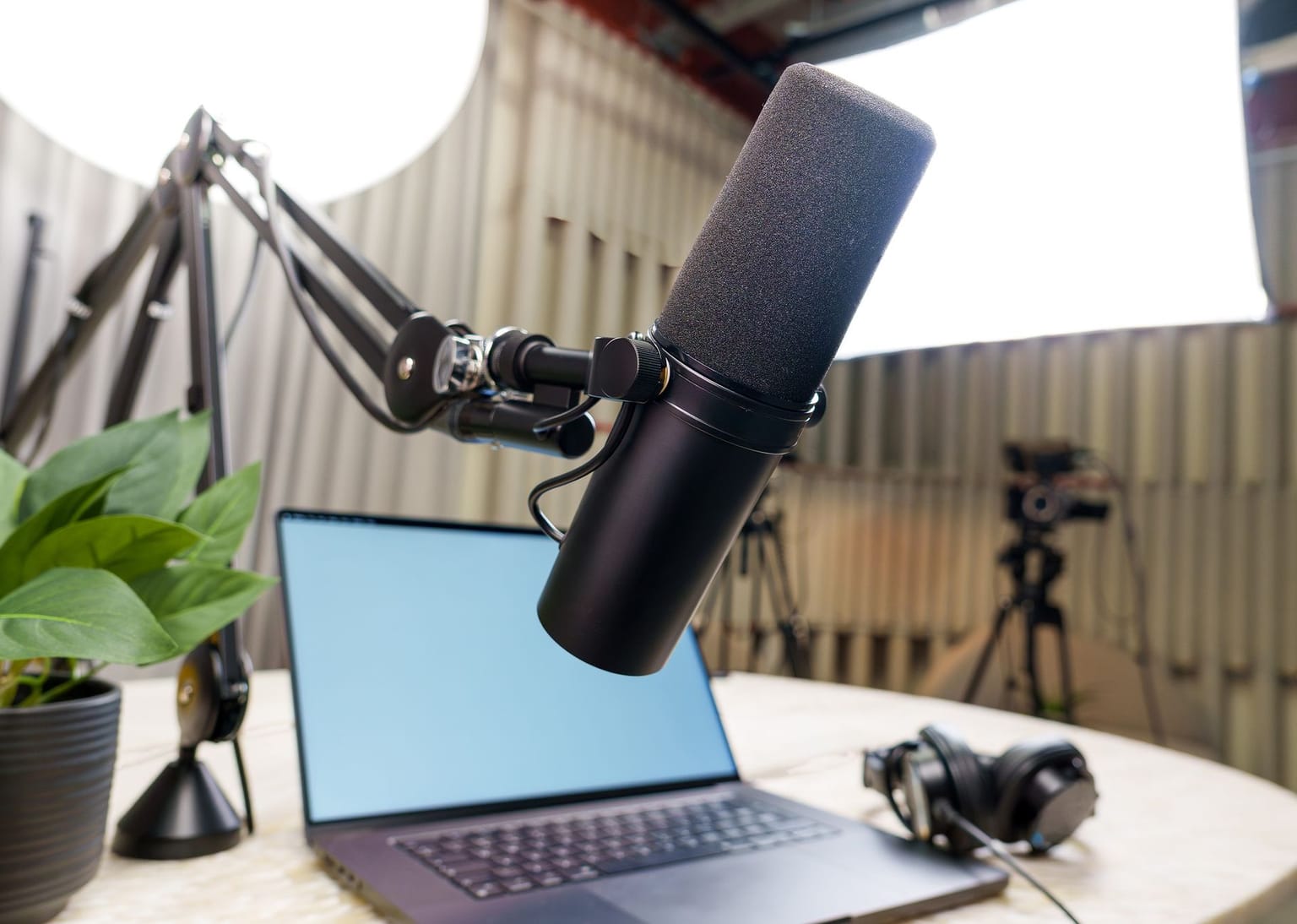 A podcast setup with a microphone on an adjustable arm, a laptop, headphones, and a potted plant on a desk creates the perfect atmosphere for content