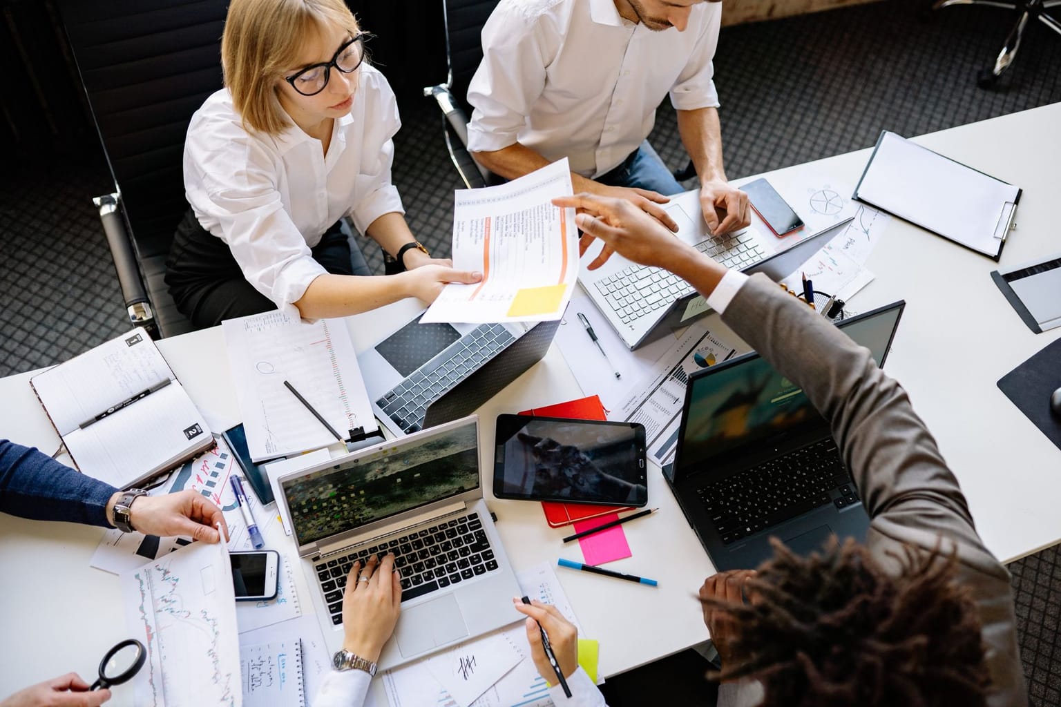 Four people from a dynamic startup team work at a cluttered desk with laptops, tablets